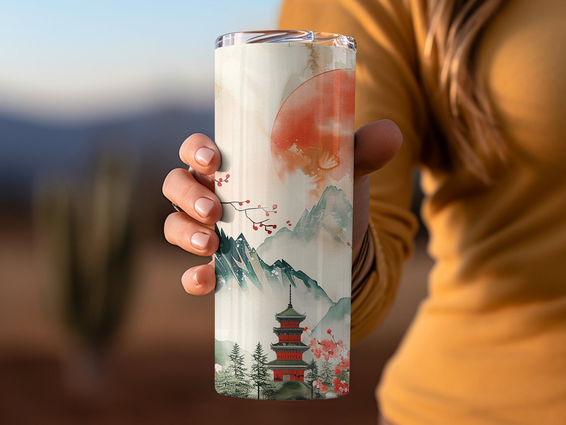 Japanese sunset tumbler in hand, 20oz stainless steel with warm sunset colours and secure clear lid