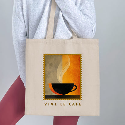 Minimalist Coffee & Steam Tote Bag held by a woman, with black cup silhouette, cream steam, gold border and VIVE LE CAFE lettering.