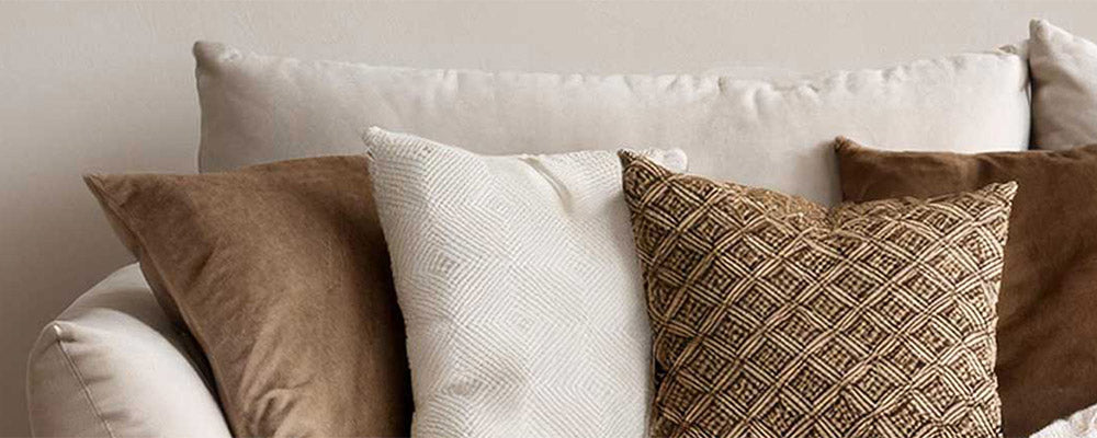 Neutral throw pillows in cream, tan and brown geometric patterns layered on a cream sofa.