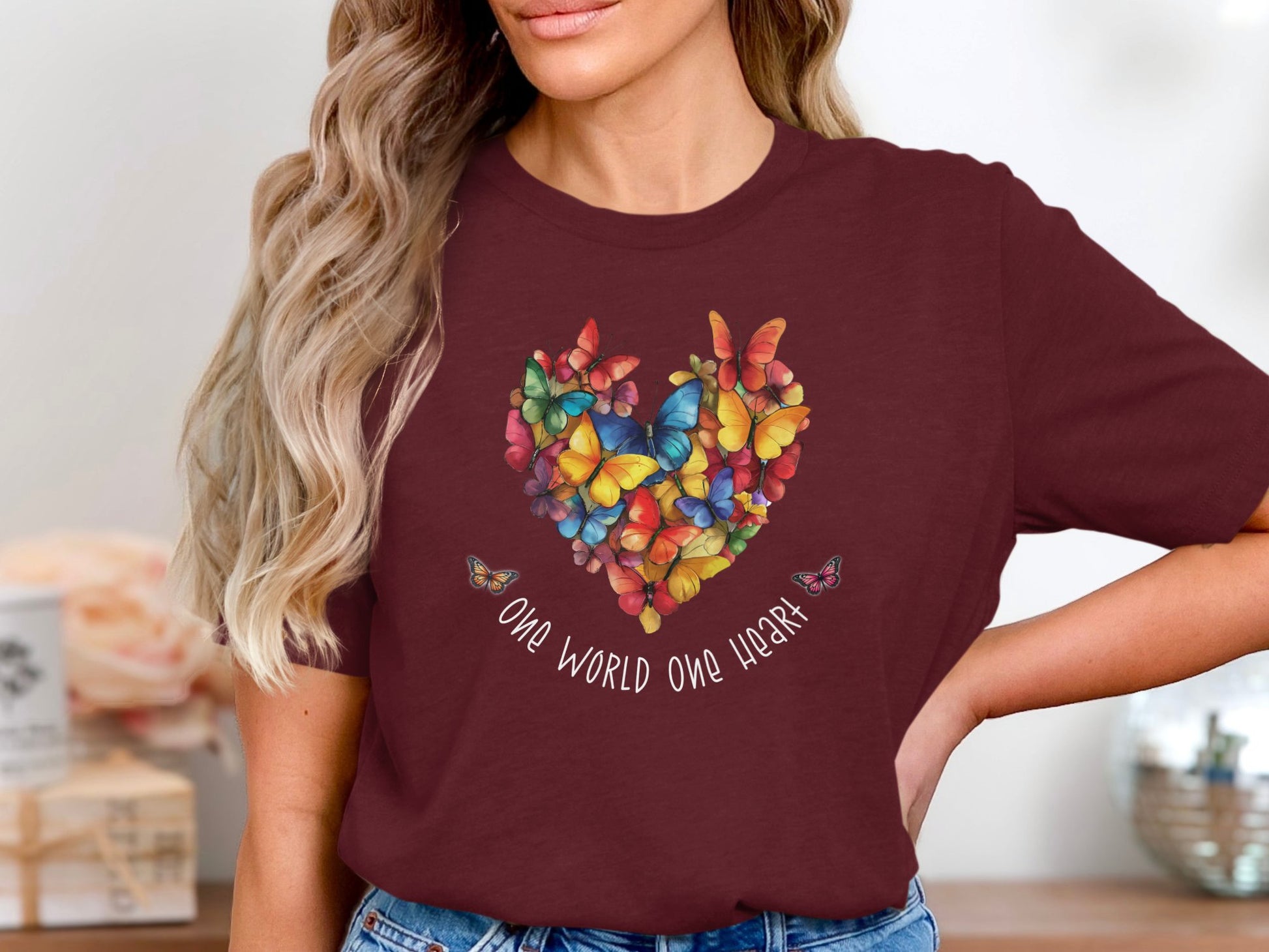 Maroon One World One Heart t-shirt with bold butterfly heart chest illustration in layered colour tones and uplifting script typography.