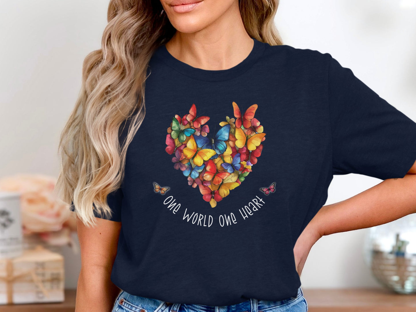 Navy One World One Heart tee with vibrant butterfly heart design across chest, painterly colour blend and soft script message below.