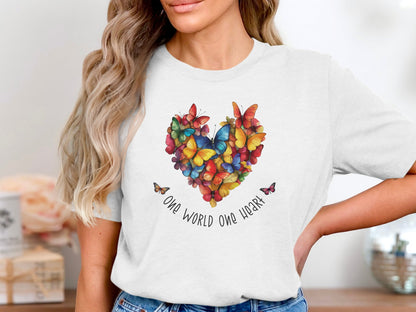 White One World One Heart t-shirt showcasing curved black script anchoring a colourful heart-shaped mosaic of butterflies at centre-chest.