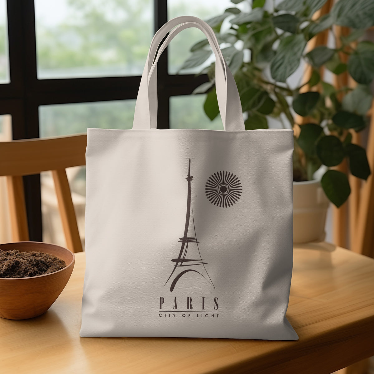 Natural canvas Paris City of Light Tote Bag on a wooden table, featuring expressive Eiffel Tower linework, CITY OF LIGHT lettering and dual handles.