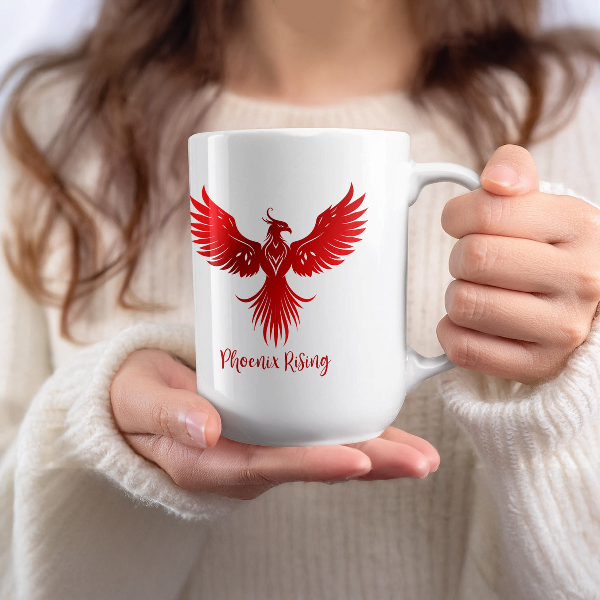 White 15oz Phoenix Rising Mug held in hand, showing the red phoenix’s closed beak, small crest and flowing tail feathers.