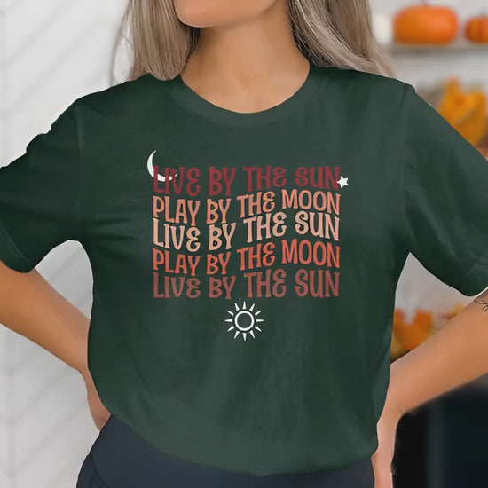 Live By The Sun Play By The Moon t-shirt showing chest mantra typography in warm retro script with sun and moon details.