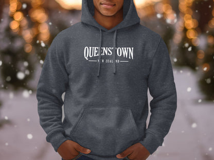Dark heather grey Queenstown New Zealand hoodie with arched lettering and vintage travel souvenir-style chest graphic.