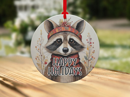 Nature-inspired raccoon ornament with expressive eyes, botanical details, and cheerful Happy Holidays text.