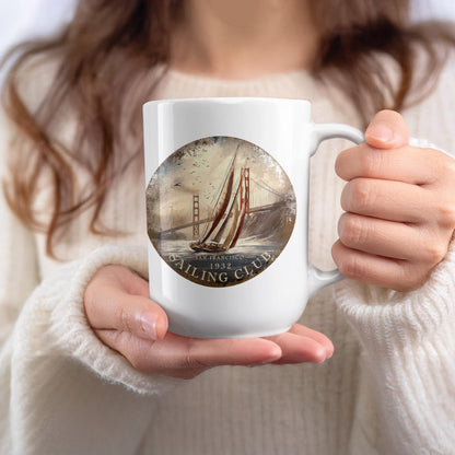 White 15oz San Francisco Sailing Club Mug held in hand, showing the sailing yacht, rust-red bridge and warm sepia tones.