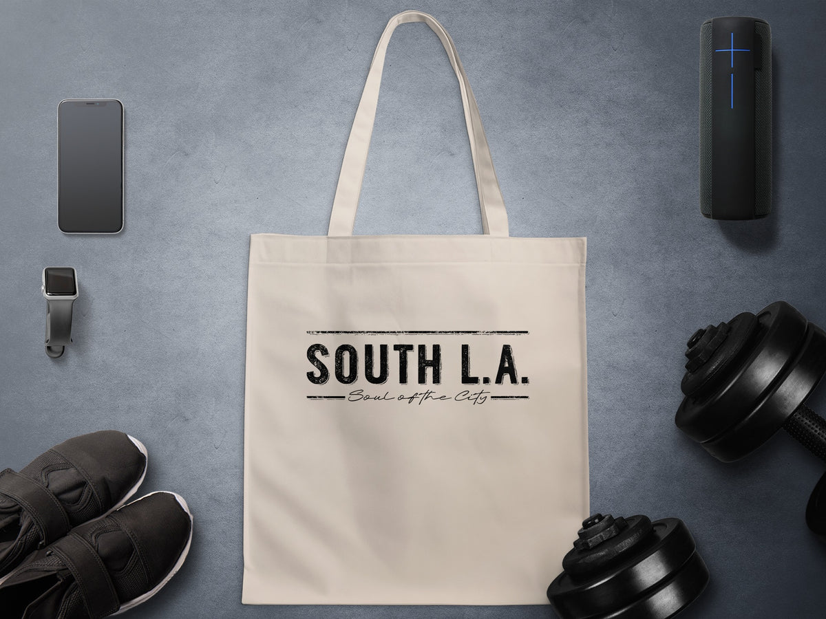 Natural canvas South L.A. Soul of the City tote bag with fine black handwritten script beneath bold uppercase lettering and horizontal rules.