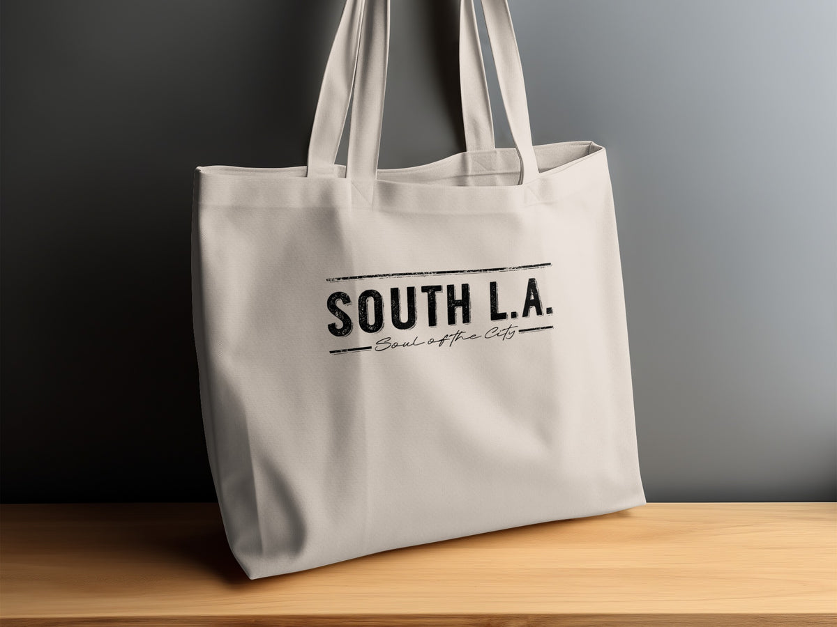 Close-up of the South L.A. tote bag on a sideboard showing bold black lettering with a lightly distressed texture.