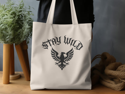 Natural-tone Stay Wild Heraldic Eagle Tote Bag in a lifestyle setting, highlighting the bold monochrome graphic and cotton canvas.