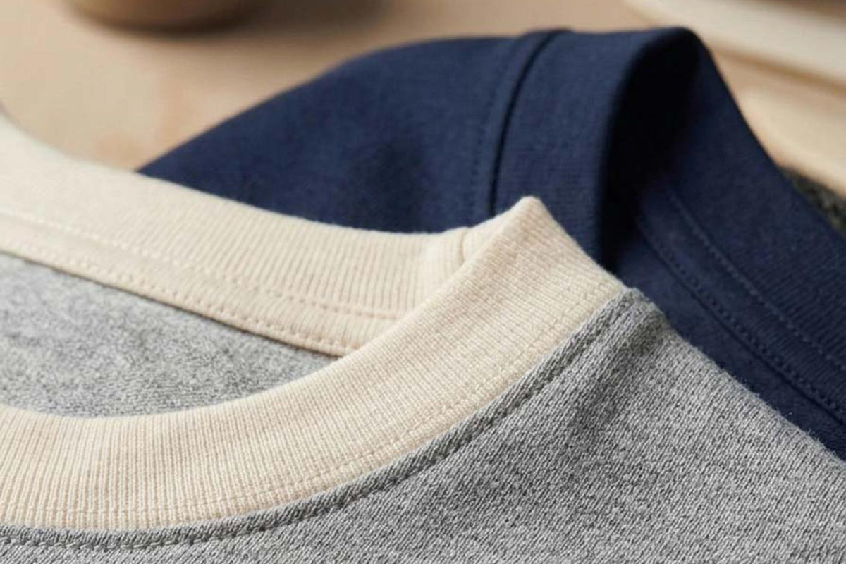 Close-up of heathered crewneck sweatshirt fabric showing soft texture and ribbed collar construction in heather grey and navy.