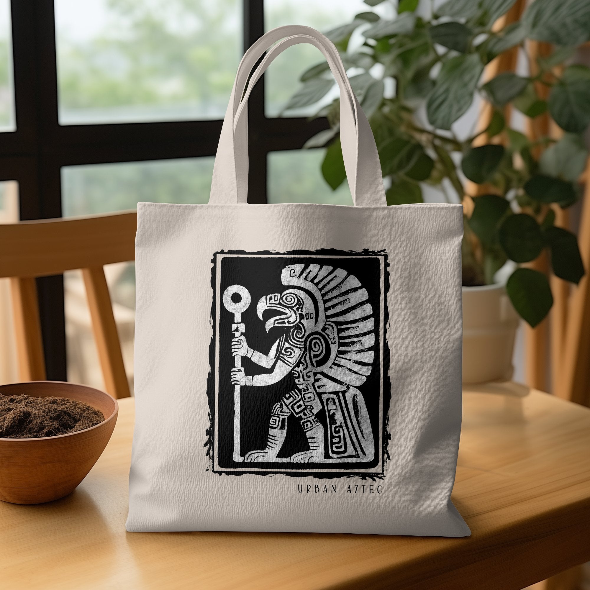 Urban Aztec Tote Bag Edition 3 displaying an Aztec warrior figure with geometric patterning and ceremonial staff, placed on a wooden table.