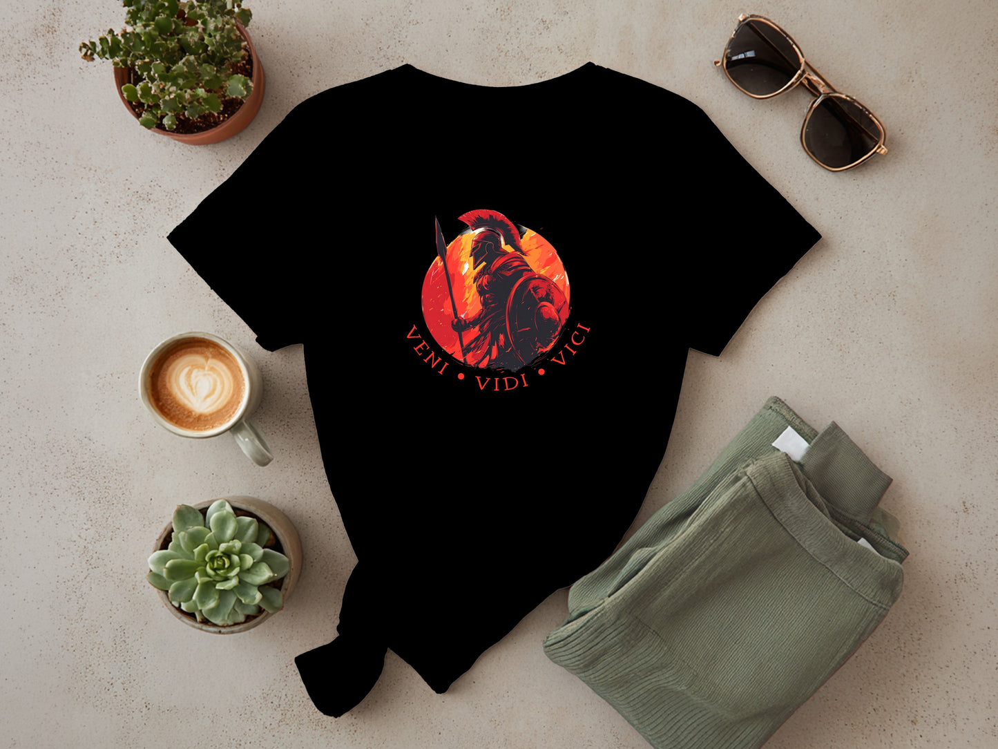Flat lay of black Veni Vidi Vici T-shirt showing centre-chest Roman warrior graphic and circular Latin red toned typography design.