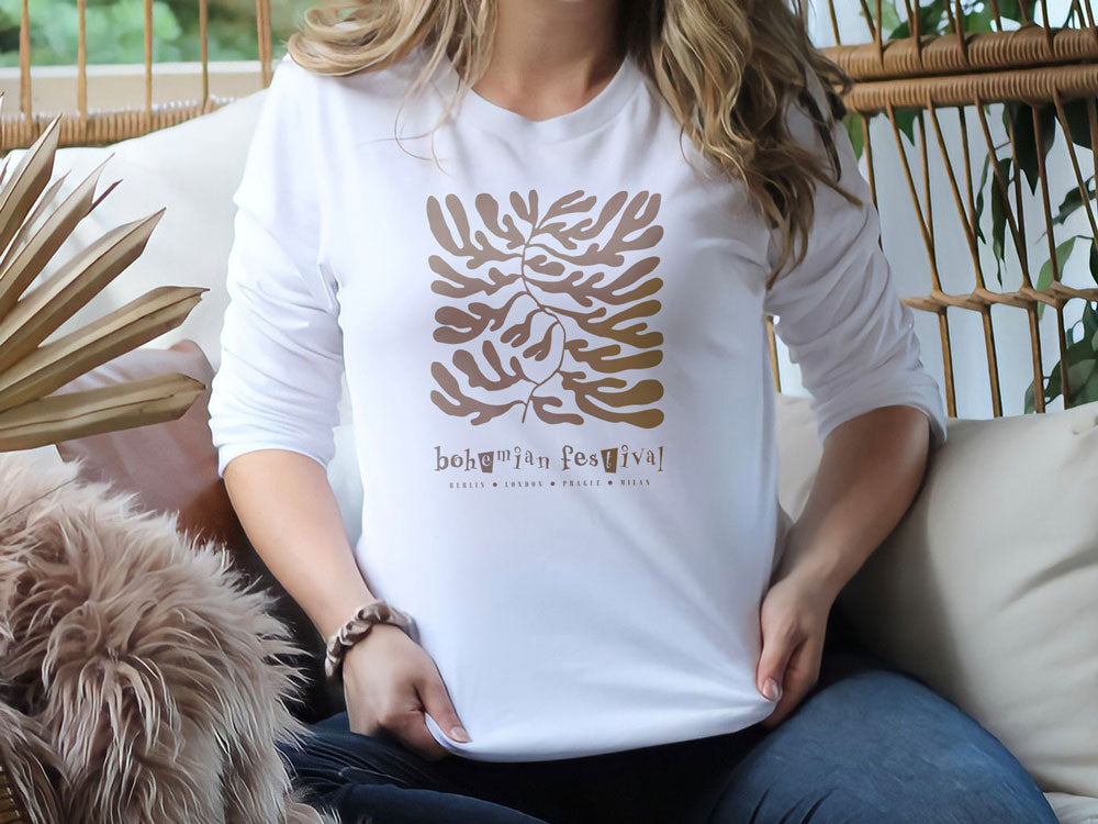 Woman wearing a white long sleeve sweatshirt with rolled sleeves, featuring gold botanical Bohemian Festival graphic print.
