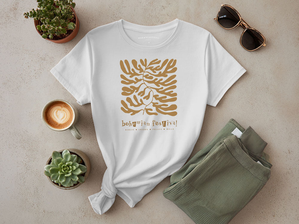 White boho graphic t-shirt with gold botanical festival print, styled with sage green pants, coffee, and succulents.