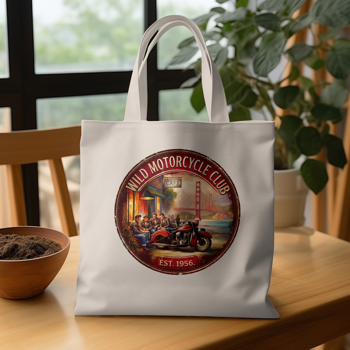 Wild Motorcycle Club Tote Bag on a wooden table, featuring bikers outside a roadside cafe with the Golden Gate Bridge behind them.