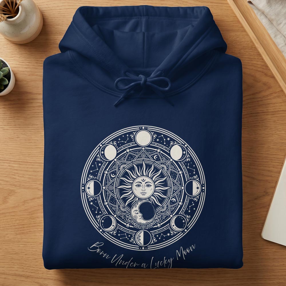 Folded navy women's hoodie featuring a white celestial sun, moon phases, and mandala graphic with 'Born Under a Lucky Moon' curved script.