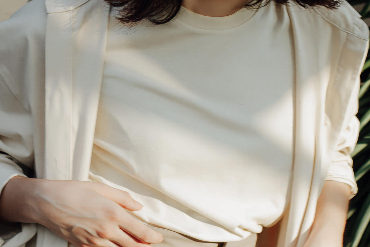 Woman wearing a tucked-in cream crew neck t-shirt layered beneath a white blazer for a smart-casual outfit.