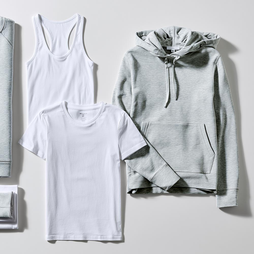 Flat lay of a white racerback tank top and crew neck t-shirt styled beside a grey marl pullover hoodie.
